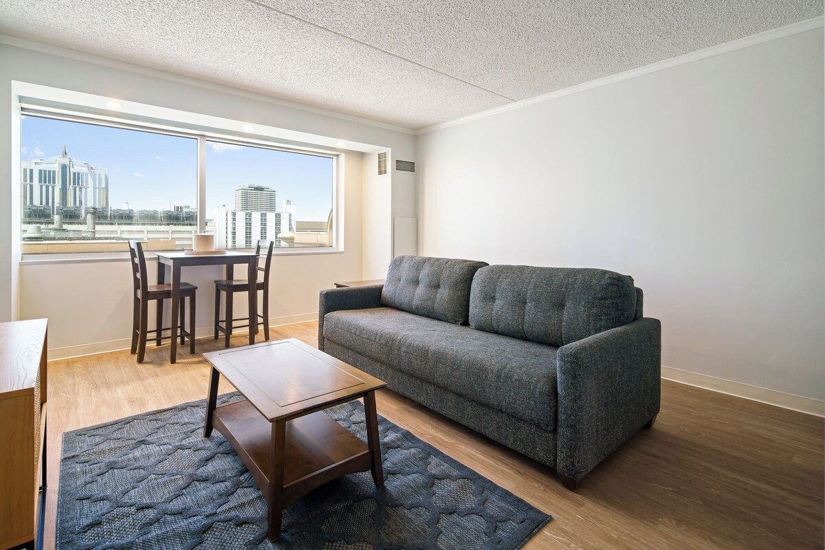 A modern living room with a gray sofa, wooden coffee table, and a dining area with chairs and a table.