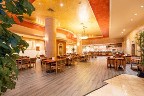 Un restaurant spacieux avec des tables et des chaises en bois, un plafond haut doté d’un éclairage encastré et une colonne centrale.