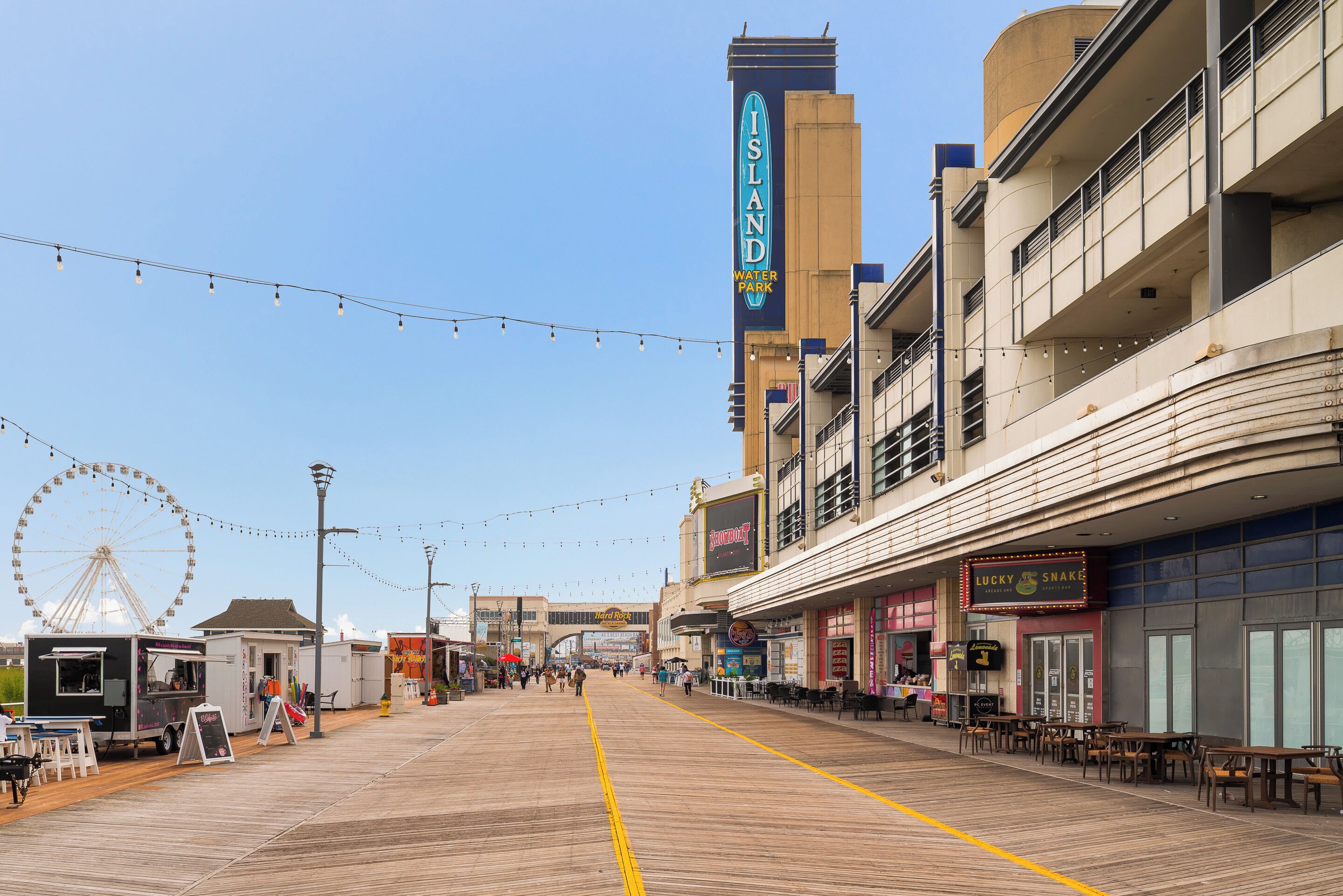 Un paseo marítimo con tiendas, una noria y un cartel de parque acuático.