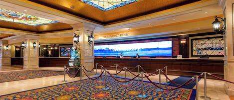 A hotel lobby with a large stained glass ceiling, a reception desk, and a patterned carpet.