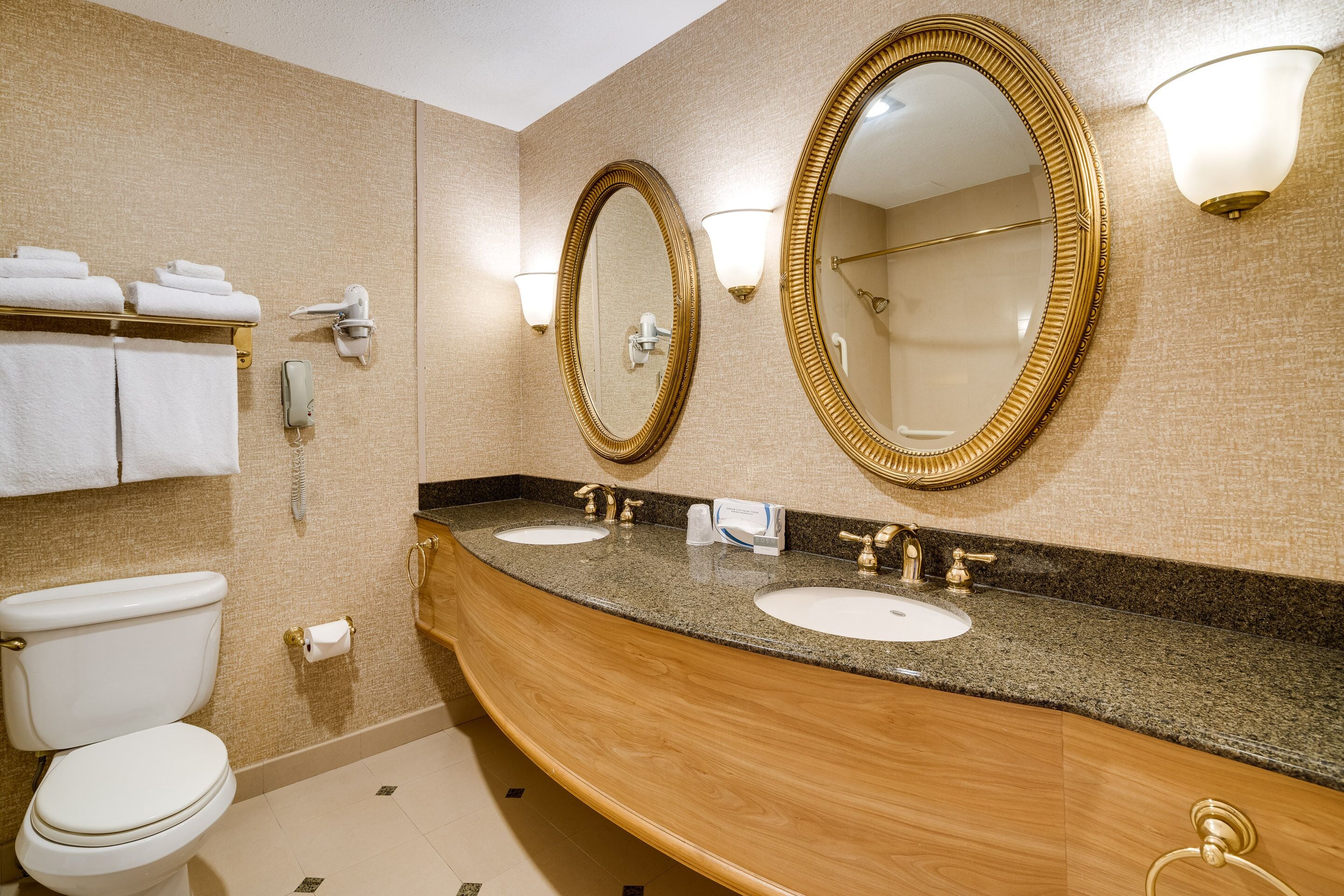 Ein Hotelbad mit zwei Waschbecken, einer Toilette und zwei großen Spiegeln mit Goldrahmen.