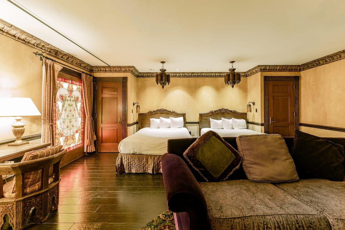 A hotel room with two beds, a sofa, a lamp, and a decorative window.