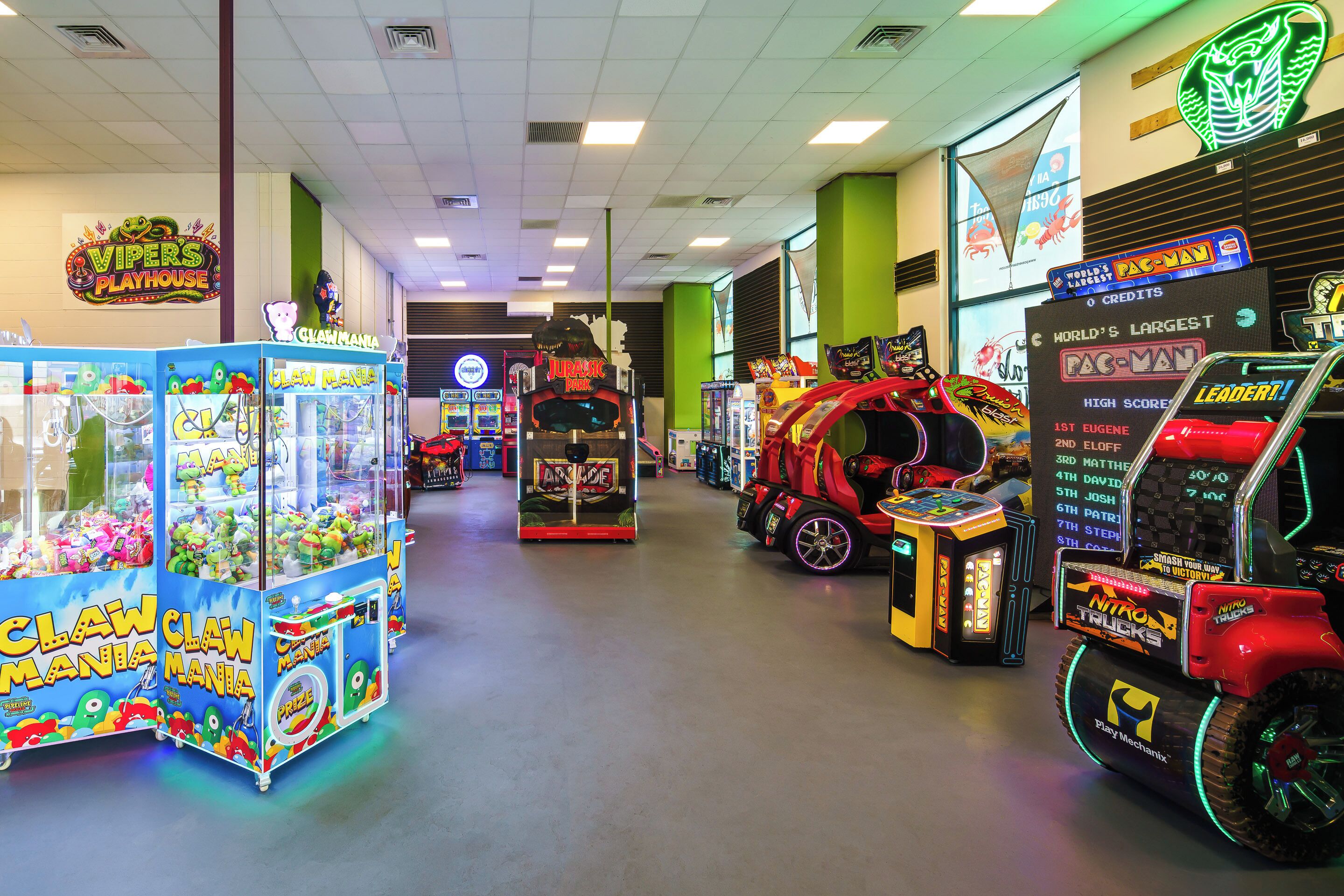 Una hilera de máquinas de garra y juegos de arcade en un espacio interior bien iluminado.