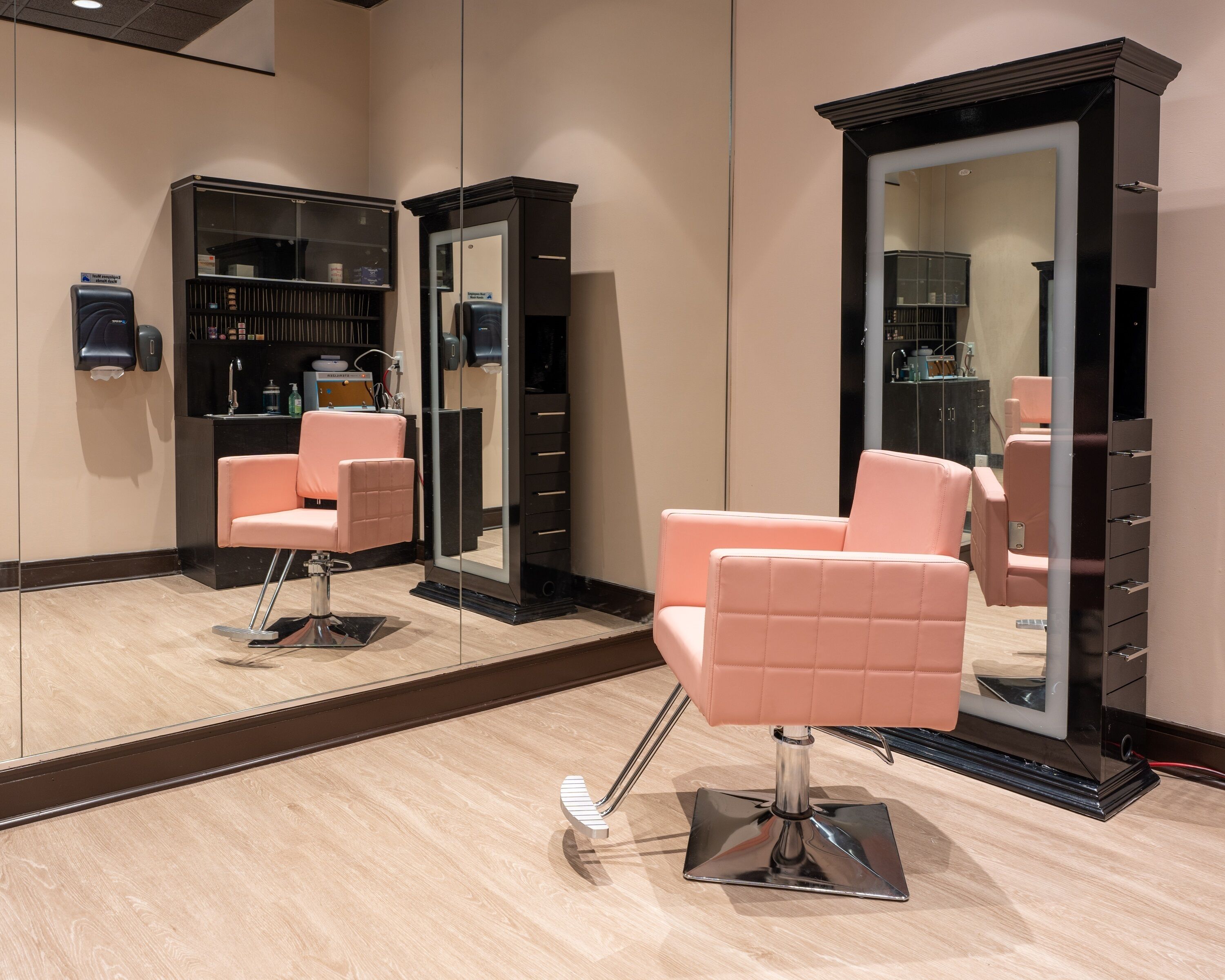 Un salon avec deux fauteuils roses, un grand miroir et un meuble noir avec des étagères.
