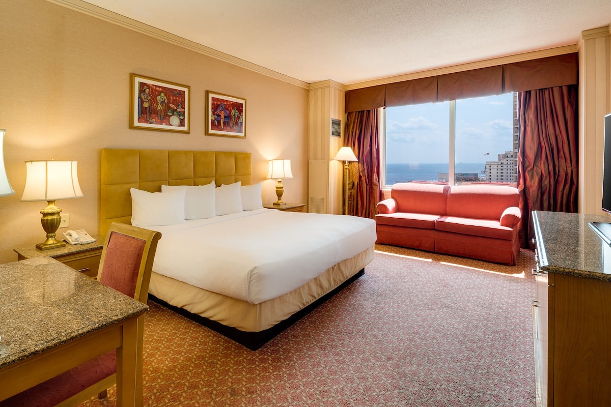 A hotel room with a large bed, a desk with a telephone, a red sofa, and a view of the ocean.
