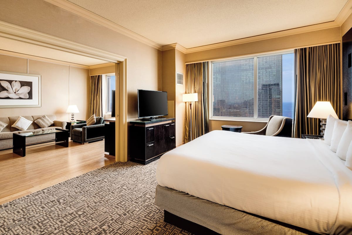 A hotel room with a large bed, a sofa, a TV, and a city view.