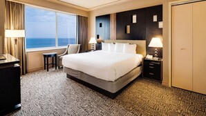 A hotel room with a large bed, a desk, a chair, a nightstand with a lamp, and a view of the ocean. - Showboat Hotel Atlantic City (Atlantic City)