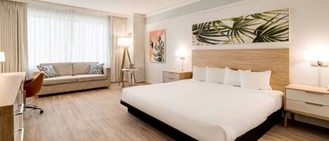 Hotellihuone, jossa on suuri sänky, sohva, työpöytä ja tuoli.