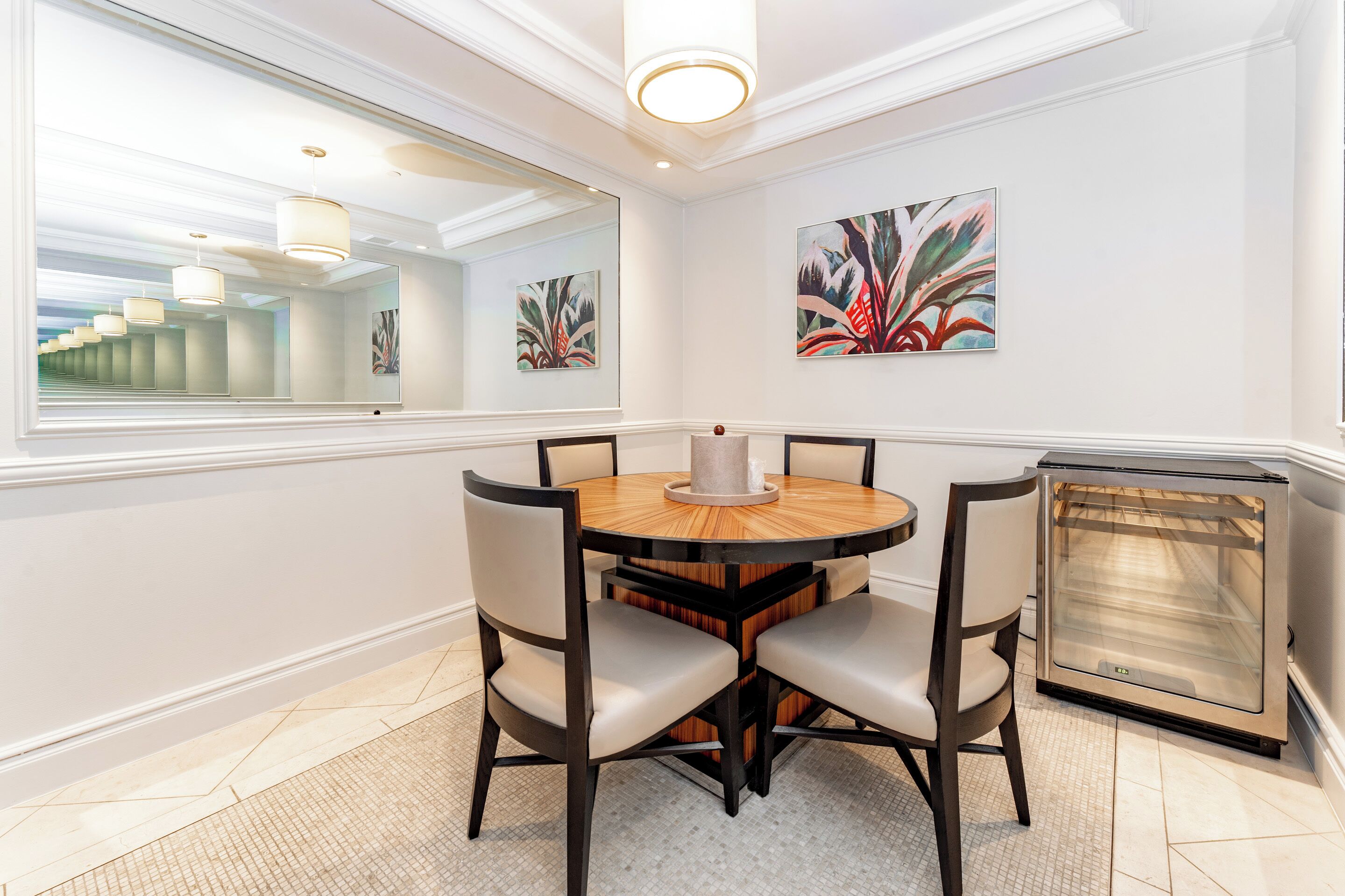 A dining area with a round table, four chairs, a central vase, and a fireplace.