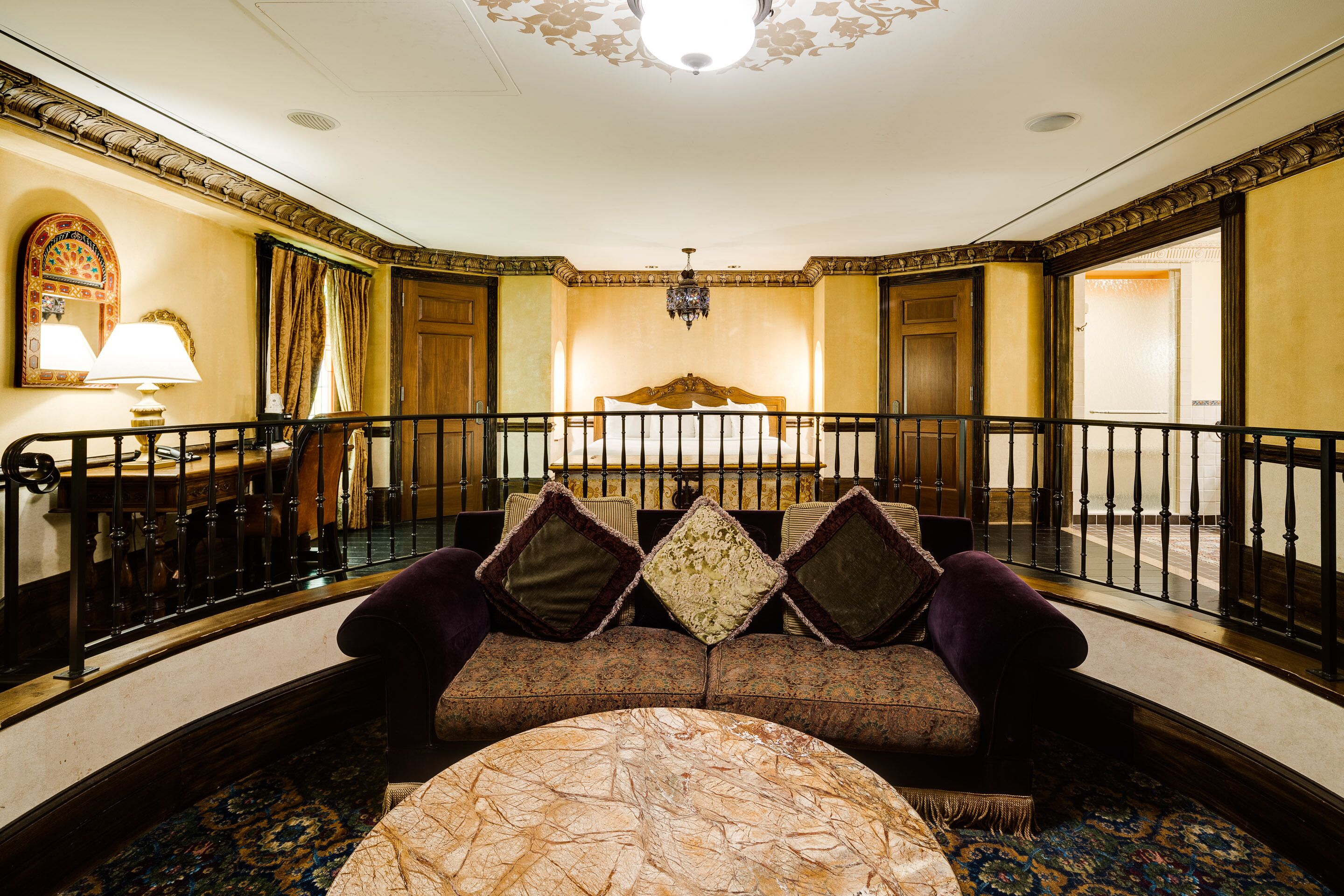 A hotel room with a balcony, a bed with a wooden headboard, a sofa with cushions, and a patterned carpet.