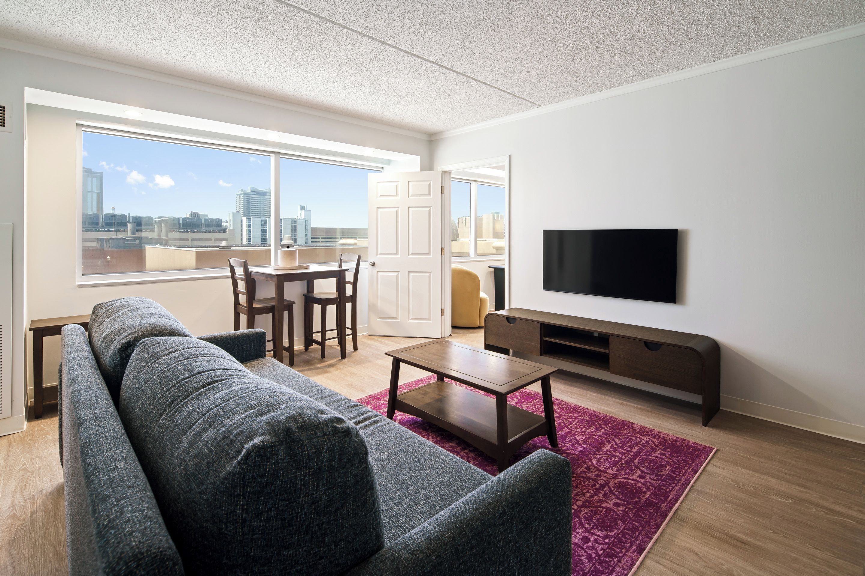 Una sala moderna con sofá, una mesa de centro, televisor y un área de comedor con sillas.