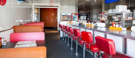 A restaurant with booths and bar seating, a Coca-Cola sign, and a kitchen area.