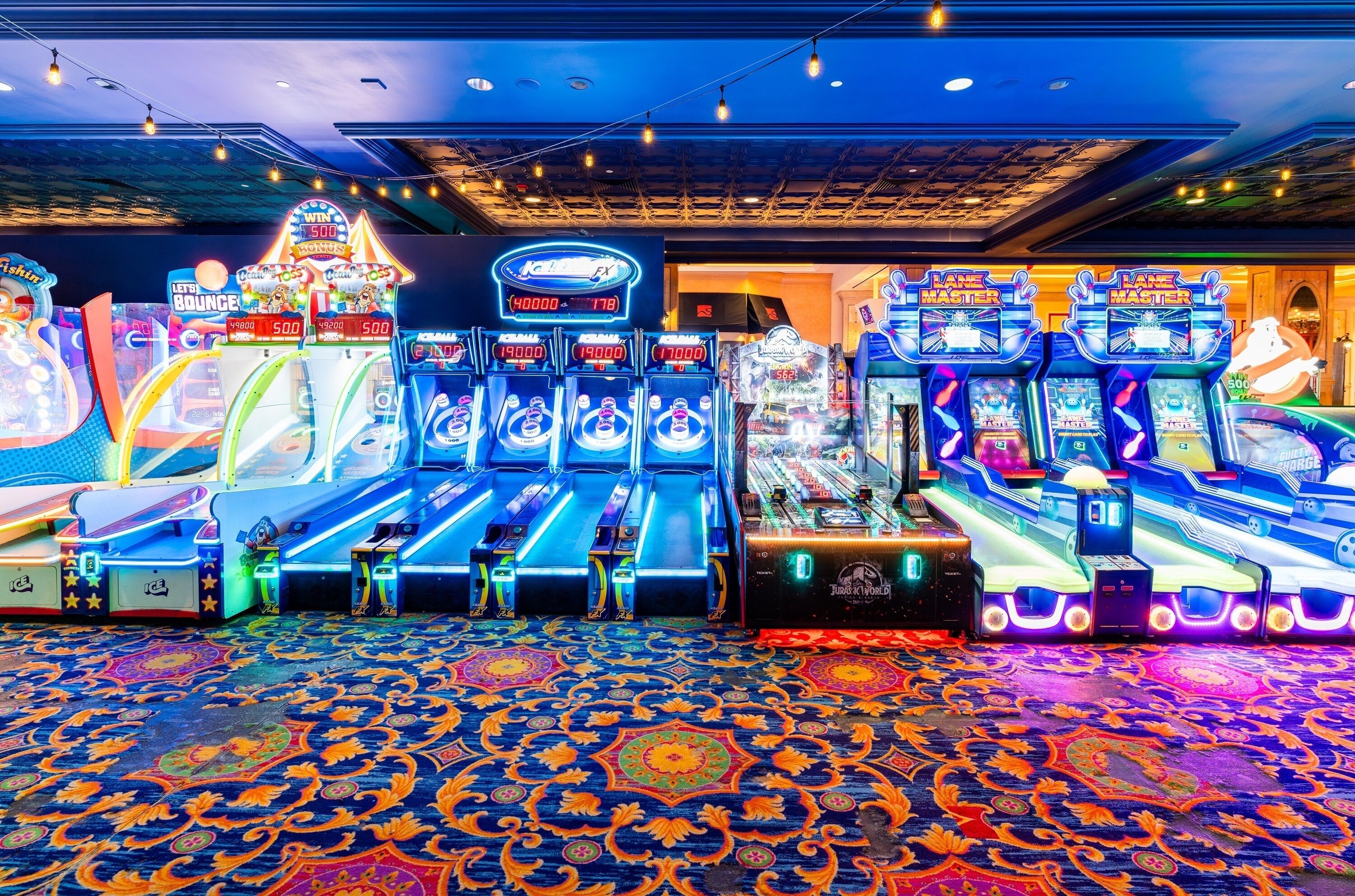 A row of arcade machines with neon lights and a patterned carpet.