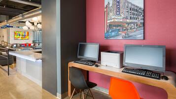 A modern office space with a long desk, two monitors, a printer, and a colorful abstract painting on the wall.
