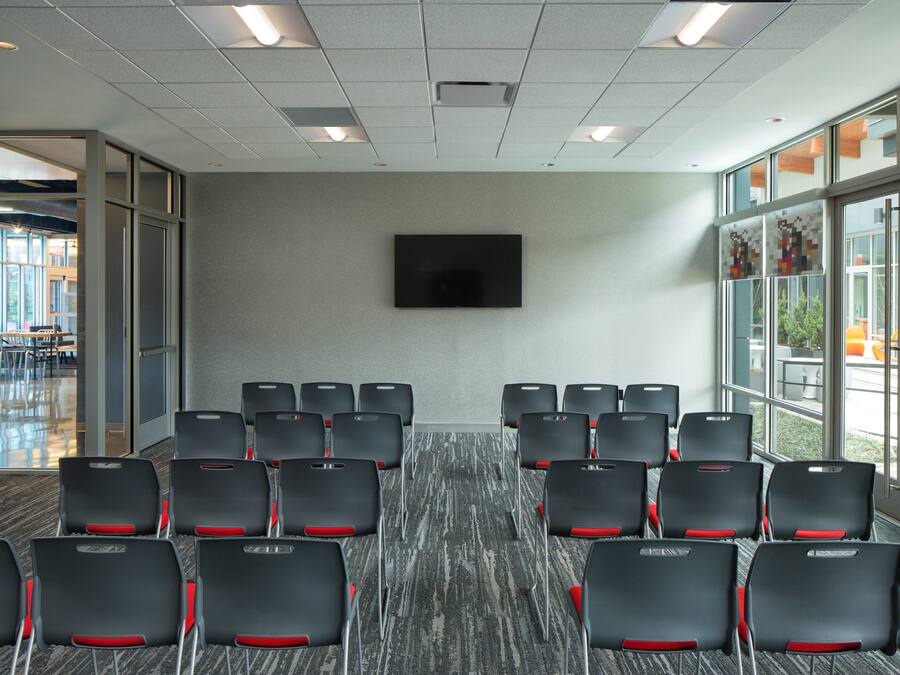 Ein Konferenzraum mit Reihen von Stühlen, einem Flachbildfernseher an der Wand und großen Fenstern mit Blick ins Freie.