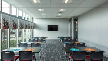 A conference room with tables, chairs, a large window, and a flat-screen TV.