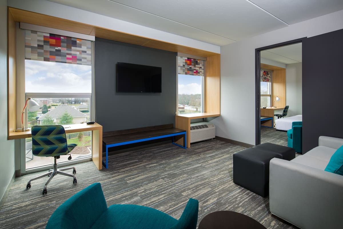 Une chambre d’hôtel moderne dotée d’une grande fenêtre, d’un bureau, d’un canapé confortable et d’un téléviseur à écran plat.