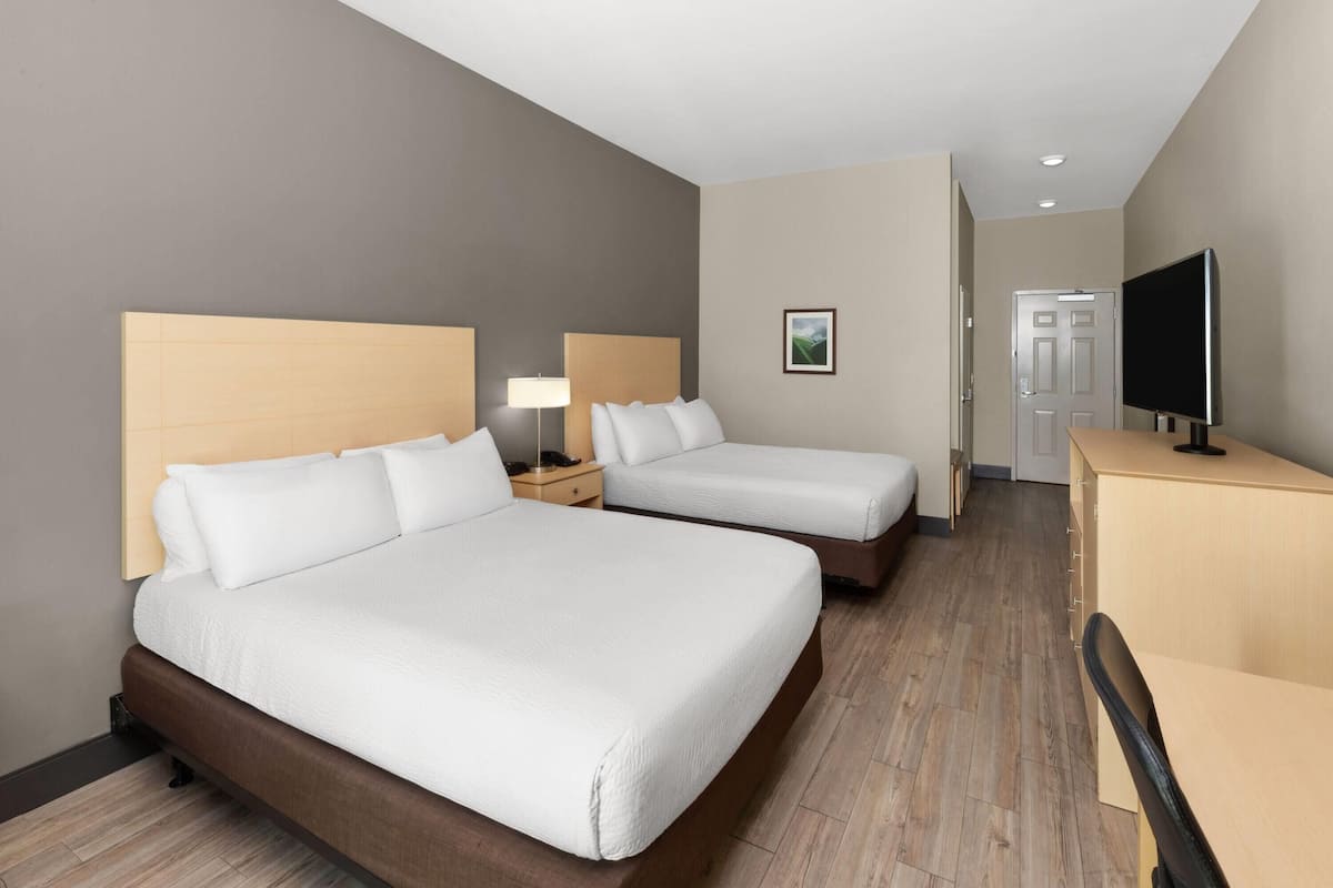 Habitación de hotel con dos camas, un escritorio, un televisor y una puerta al fondo.