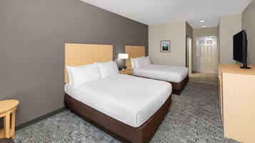 A hotel room with two beds, a desk, a television, and a door leading to another room.