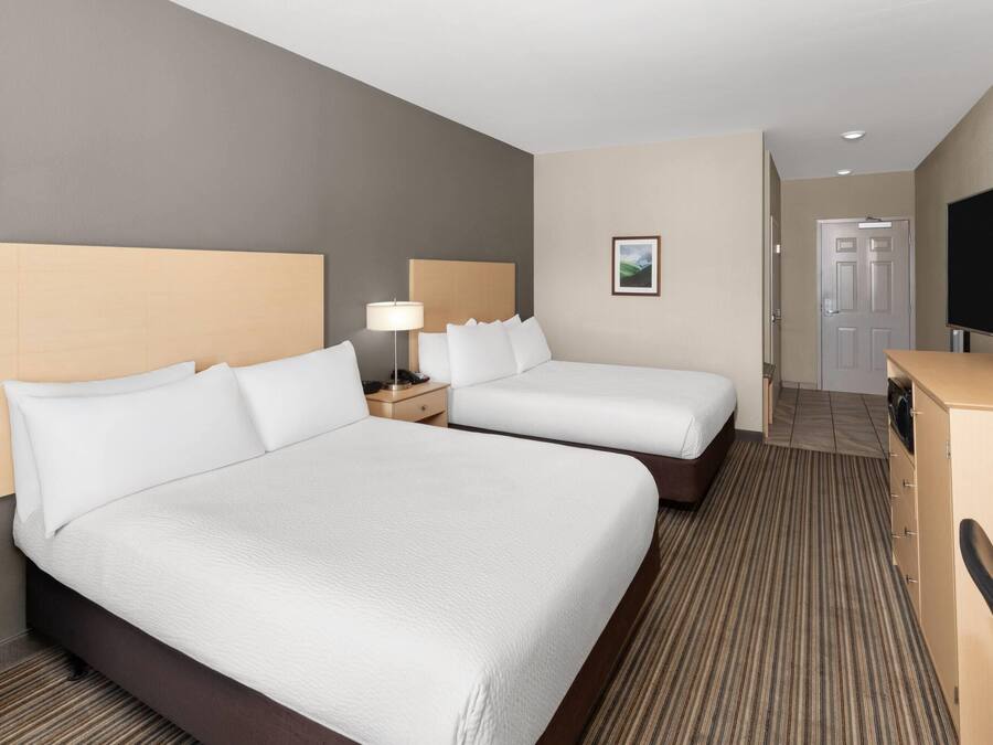 A hotel room with two beds, a desk, a television, and a door.