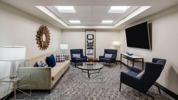 A conference room with a sofa, two armchairs, a coffee table, a TV, and a framed picture on the wall.