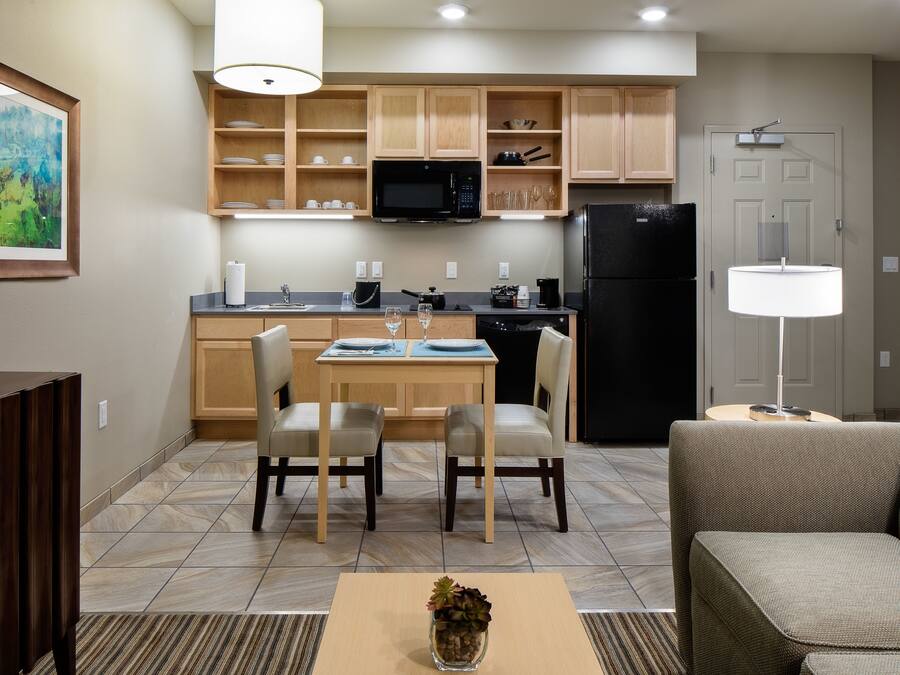 Una cocina moderna con armarios de madera, un microondas y un refrigerador. Hay un comedor con una mesa y sillas, y un sofá en la sala de estar.