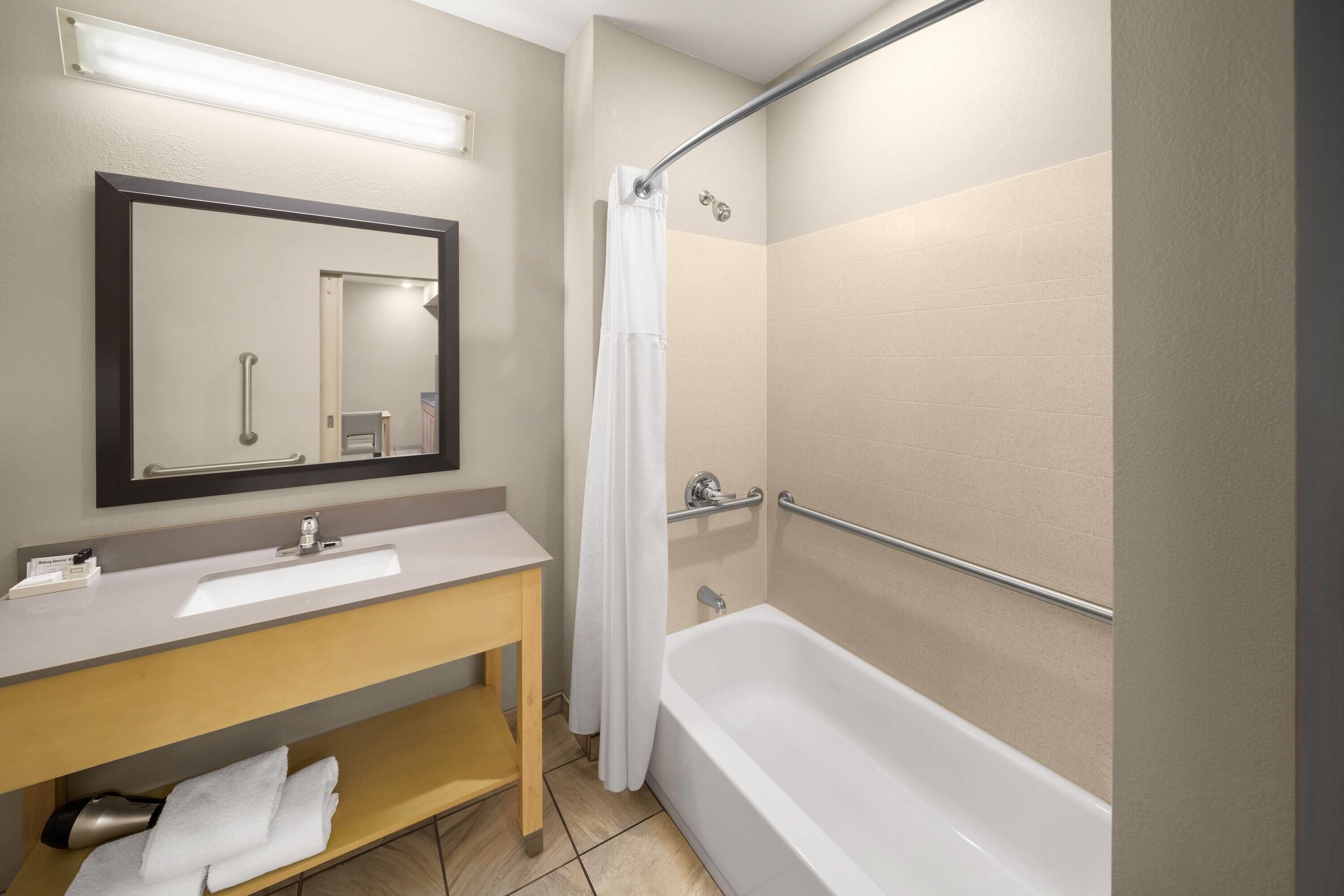 Un baño moderno con lavamanos, espejo y bañera blancos.