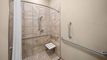 Zona de ducha con puerta de cristal, paredes con azulejos y barra de apoyo a la derecha.
