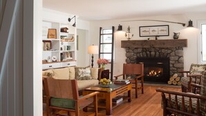 A cozy living room with a fireplace, wooden furniture, and a bookshelf filled with books and decorative items.