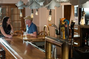 A bar area with a wooden counter, multiple beer taps, and hanging light bulbs.