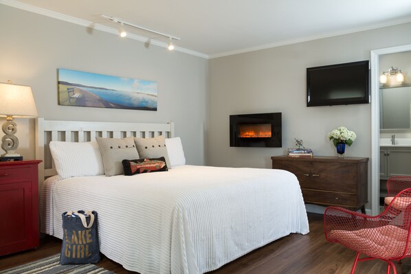 A bedroom with a bed, a TV, a fireplace, a dresser, and a chair.
