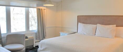 Una habitación de hotel con una cama grande, una silla, una mesita de noche y un ventanal con cortinas.