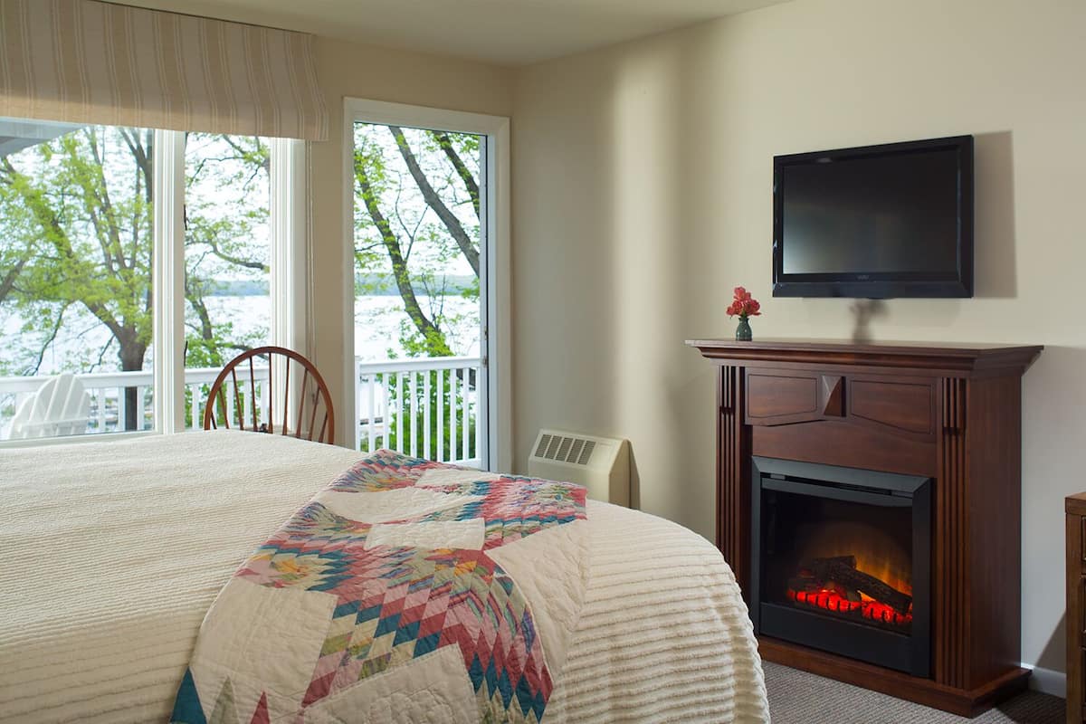 Ein Schlafzimmer mit einem großen Bett, einem Kamin, einem Fernseher und Seeblick durch das Fenster.