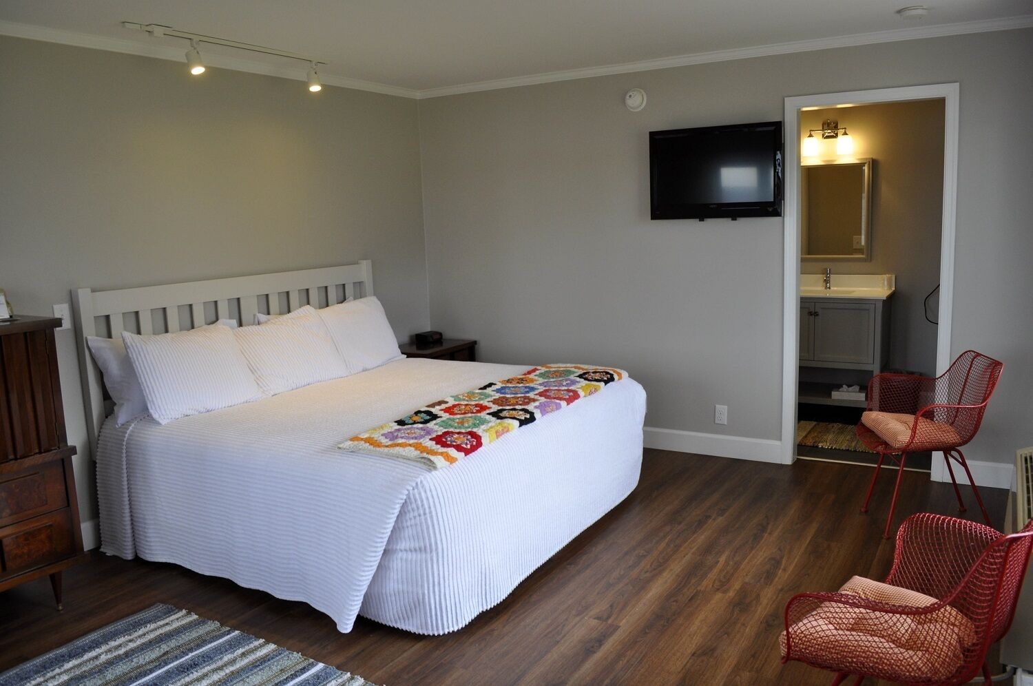 A bedroom with a bed, a quilt, a TV, a chair, and a bathroom visible through an open door.
