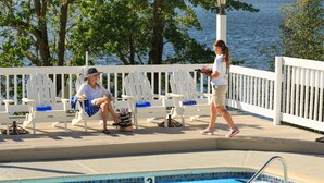 A poolside area with white Adirondack chairs, a pool, and a view of the water.