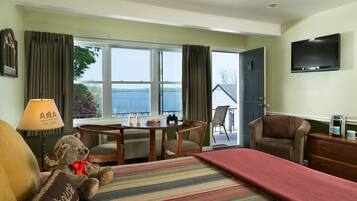 A hotel room with a bed, a desk, a chair, a television, and a view of the sea.