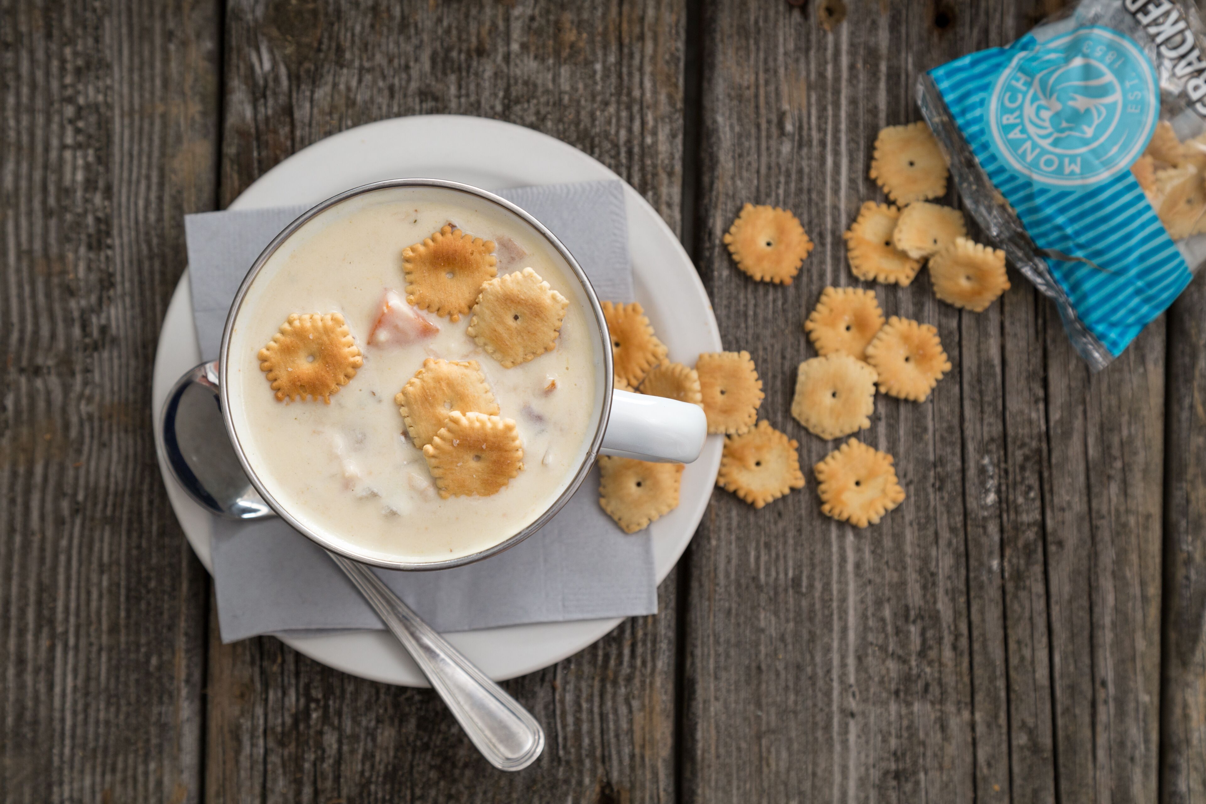 A bowl of soup with crackers on a wooden table.