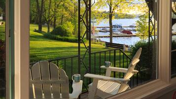 A porch with two Adirondack chairs, a small table, and a view of a lake with boats.