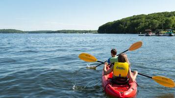 A couple kayaking on a calm lake with a forested shoreline.