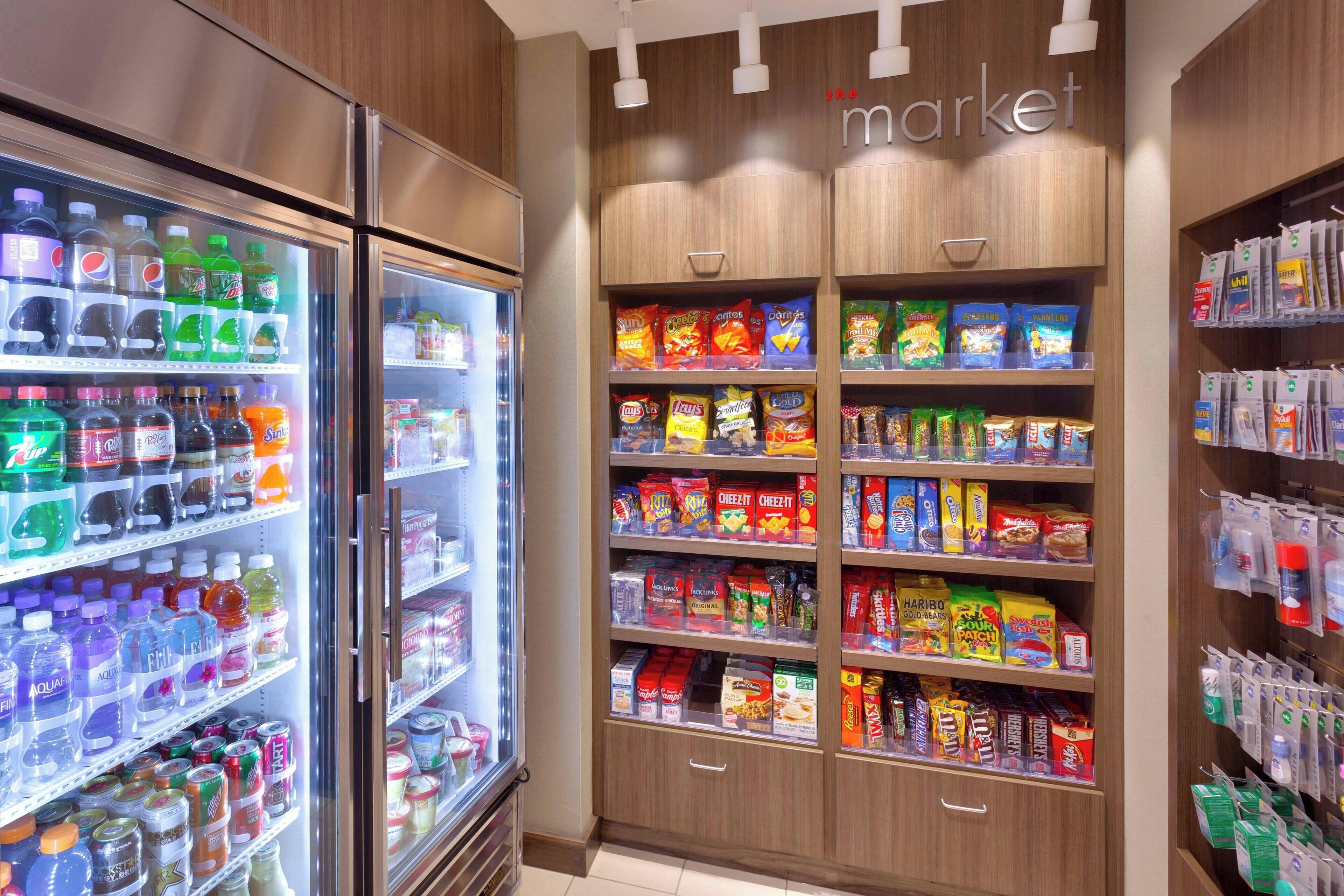 Una tienda de comestibles con bebidas refrigeradas, pasillos de bocadillos y productos envasados.