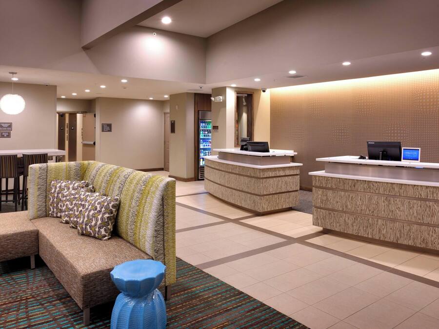 A hotel lobby with a reception desk, a seating area with a sofa and chairs, and a vending machine.