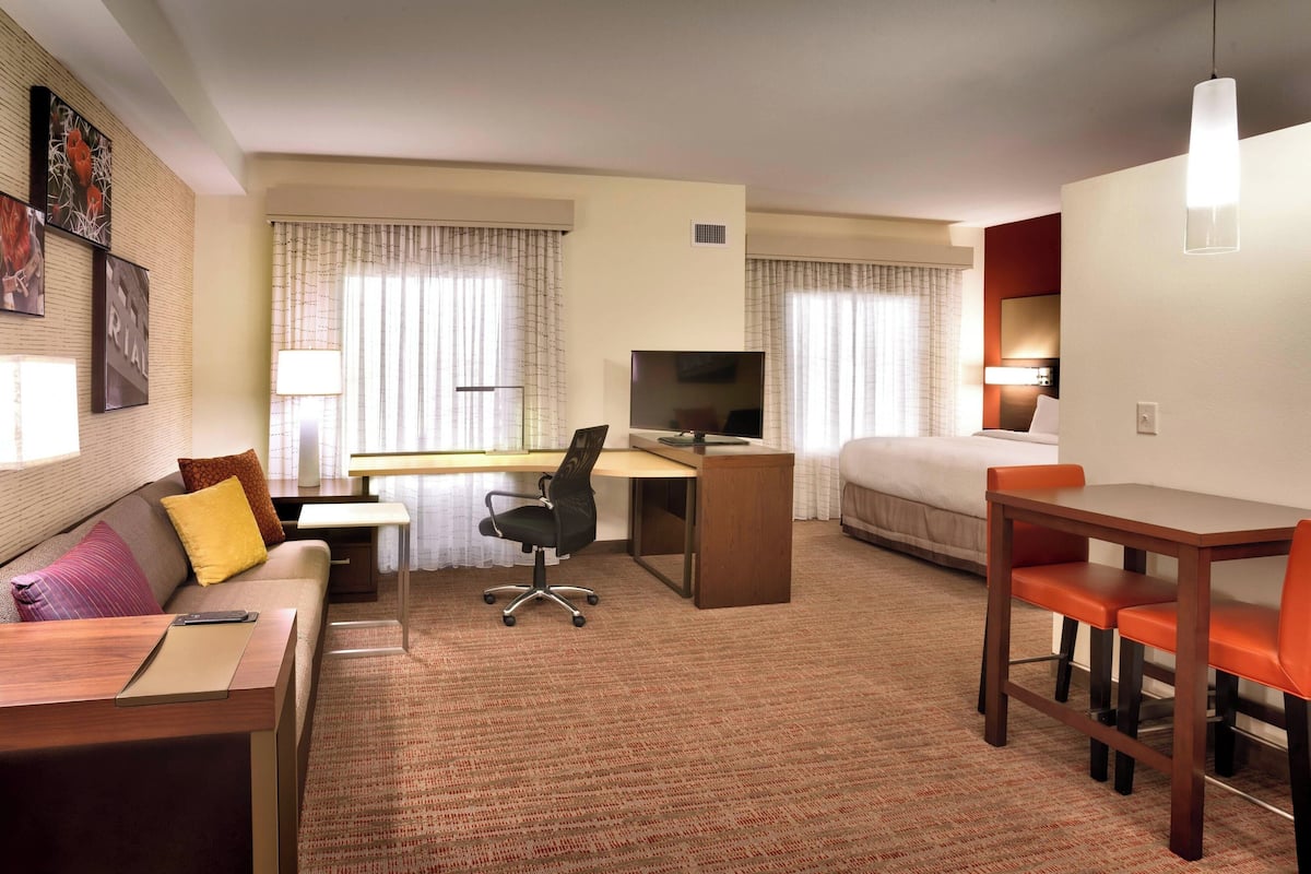 A hotel room with a bed, a desk with a computer, a TV, a sofa, and a dining table with chairs.