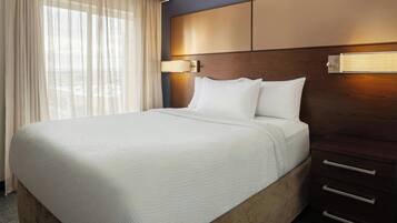 A hotel room with a large bed, a wooden headboard, a nightstand, and a window with sheer curtains.