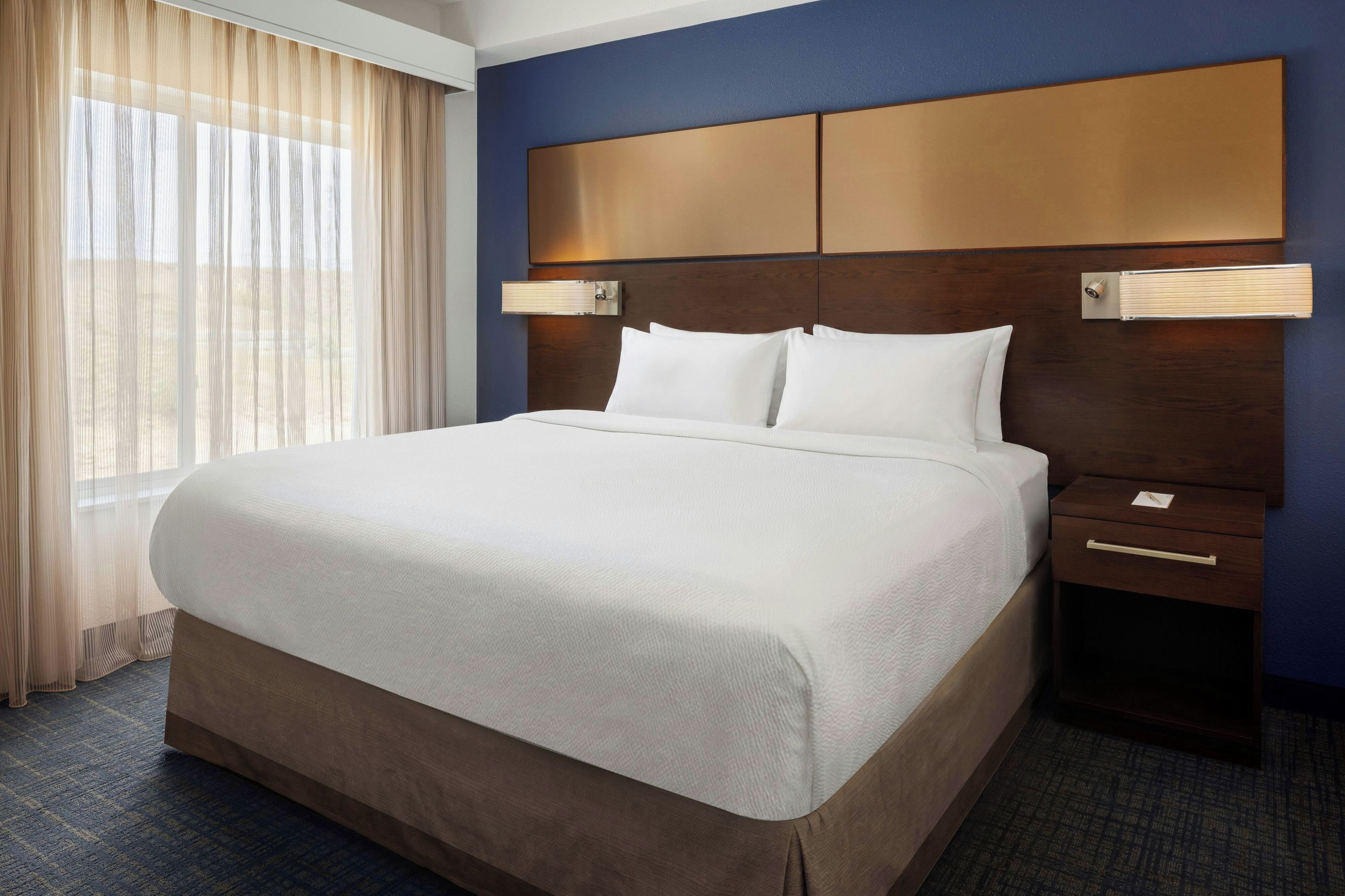 A hotel room with a large bed, a nightstand, a lamp, and a window with curtains.