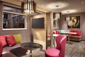 A modern hotel room with a sofa, a round table, and a pink chair. There is a flat-screen TV mounted on the wall and a painting above the sofa. - Residence Inn by Marriott Casper (Casper)