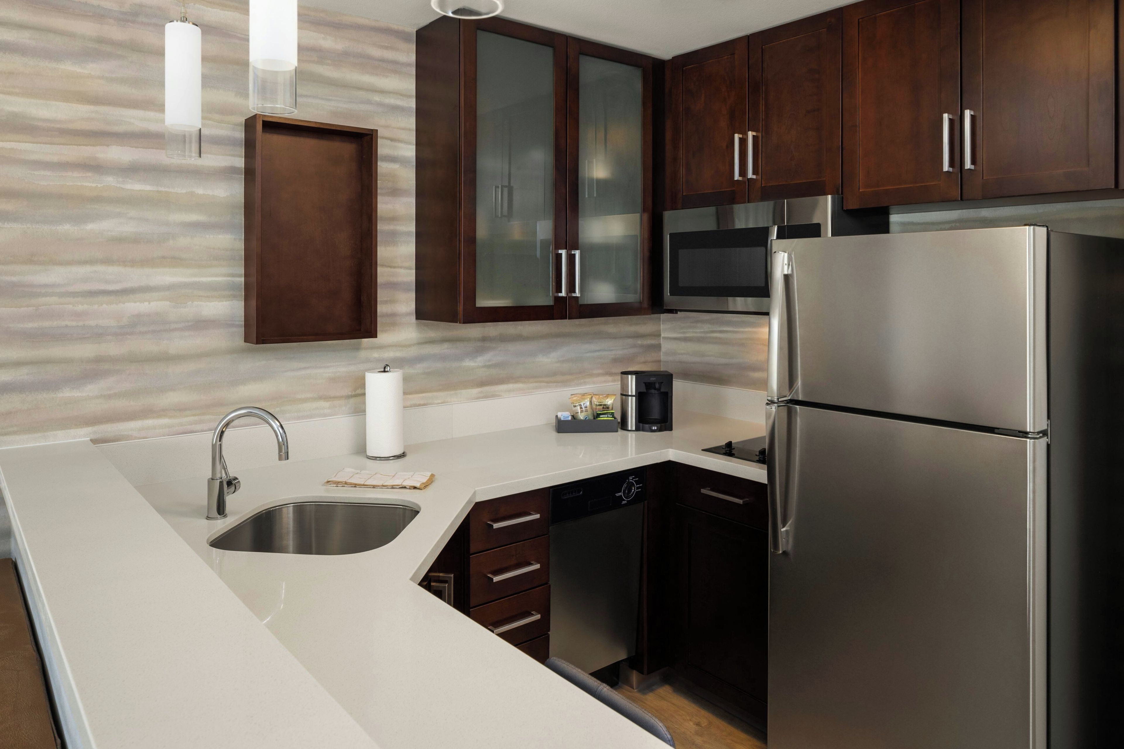 Una cocina moderna con electrodomésticos de acero inoxidable, lavavajillas integrado y armarios de madera oscura.