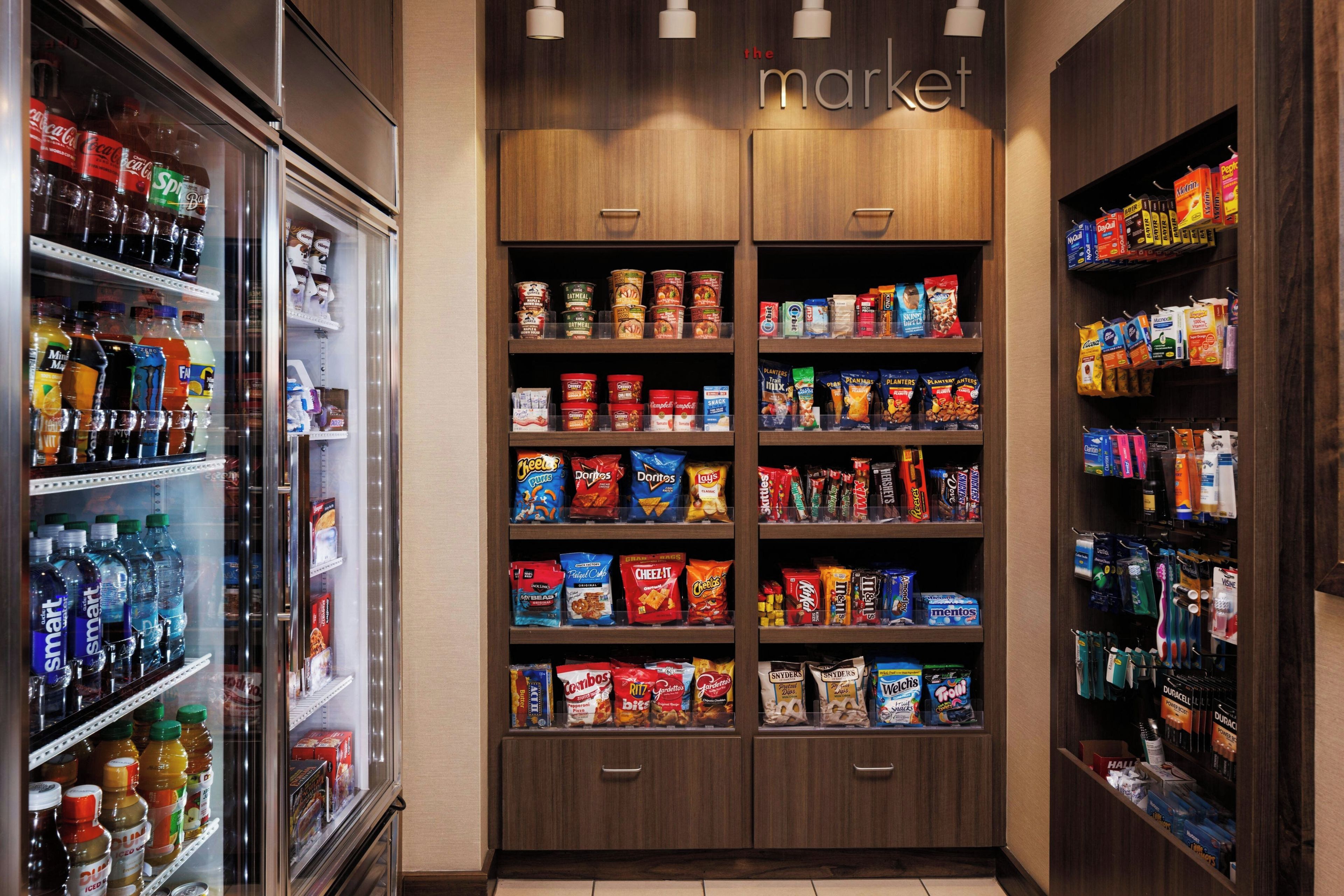 Interior de um supermercado com máquinas de bebidas refrigeradas, corredores de lanches e uma variedade de produtos embalados.