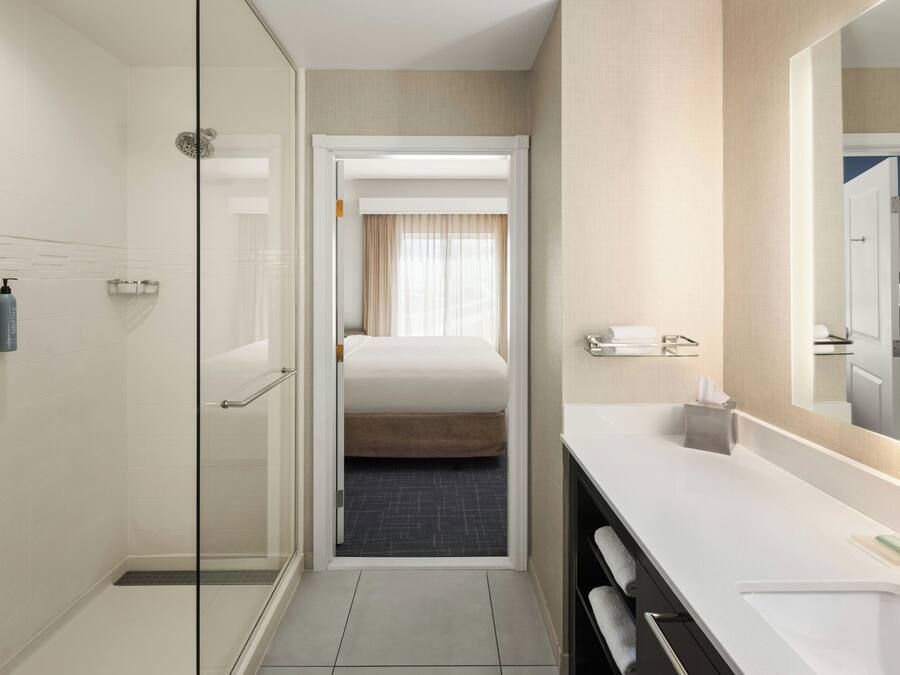 Un baño de hotel con ducha, cama, lavamanos y espejo.