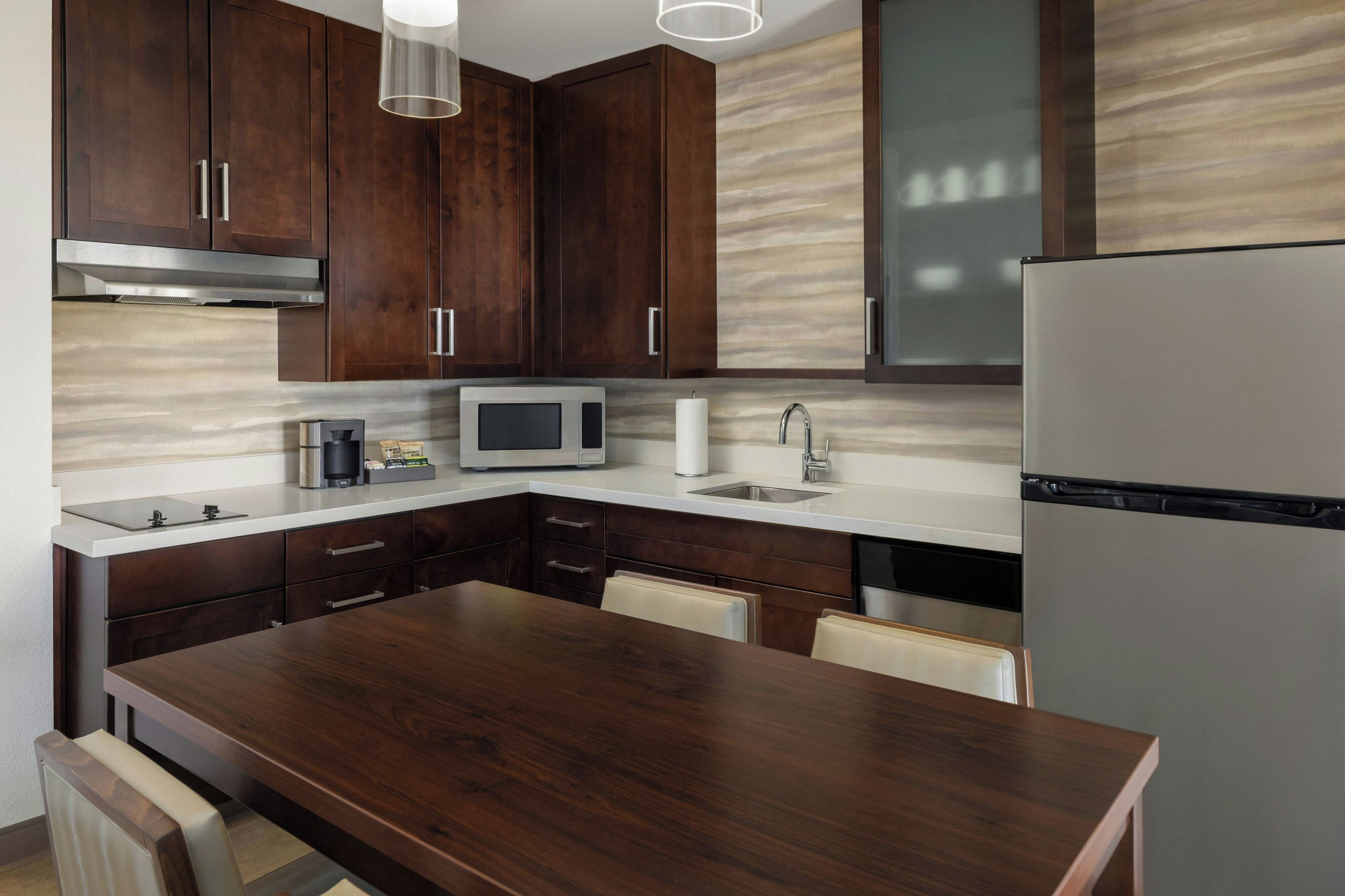 A modern kitchen with dark wood cabinets, a stainless steel refrigerator, a microwave, and a built-in oven.