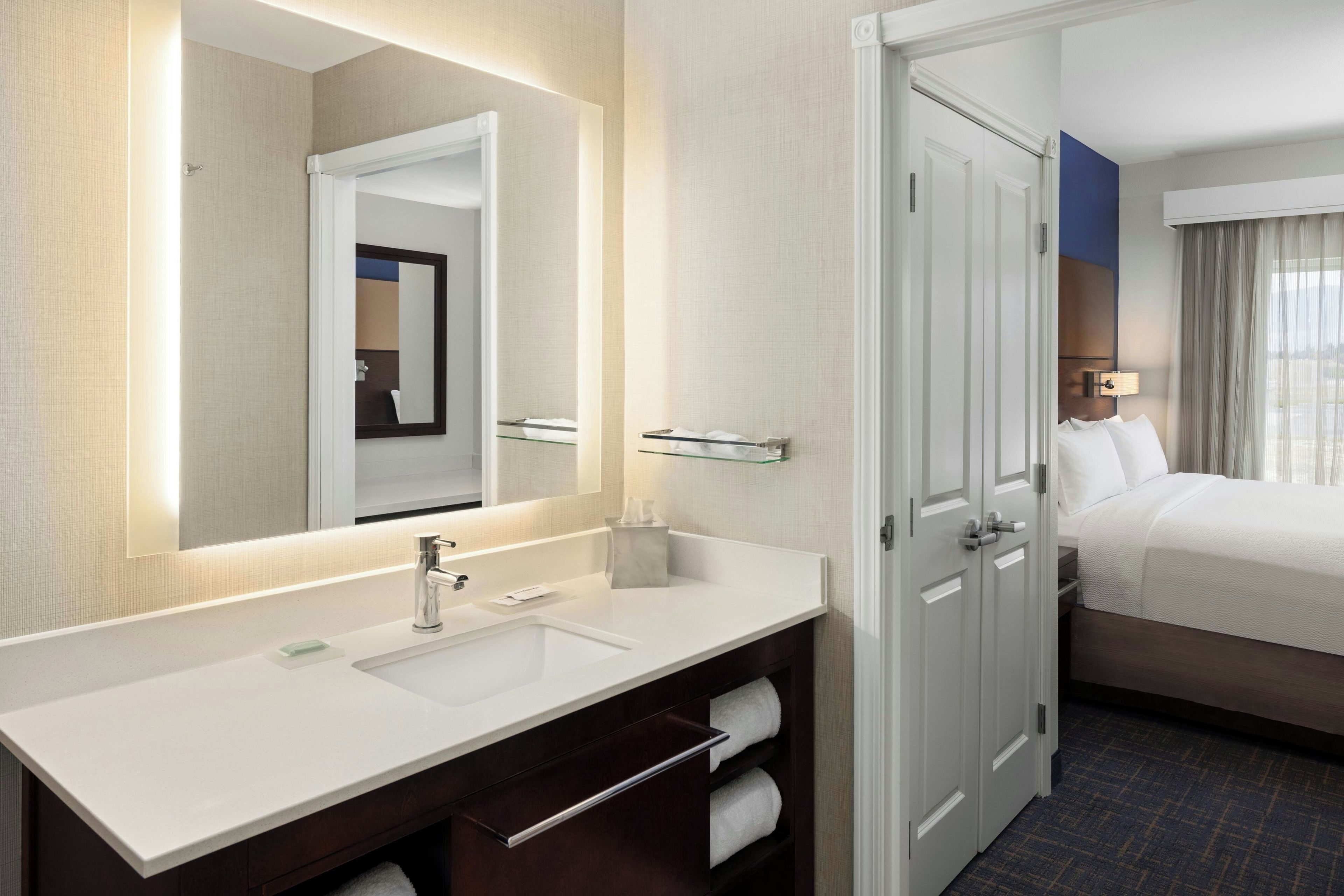 A hotel bathroom with a large mirror, a sink, and a towel rack.